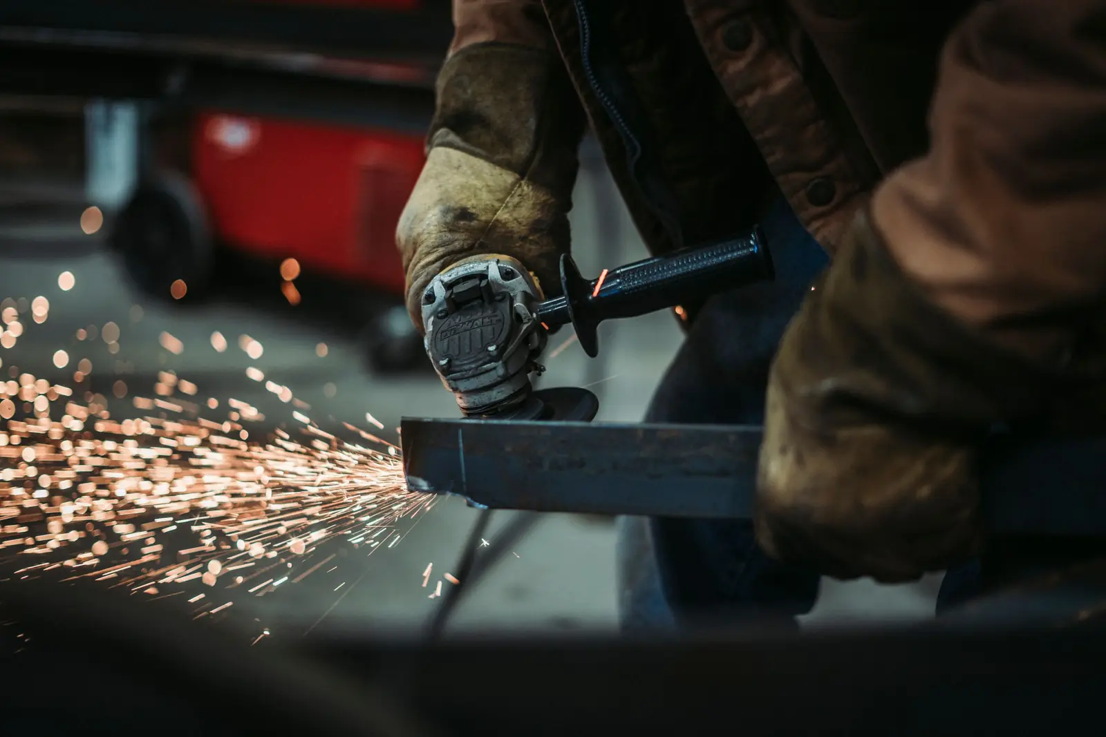 Gloved hands running an angle grinder along a steel section, throwing a wide spray of sparks.