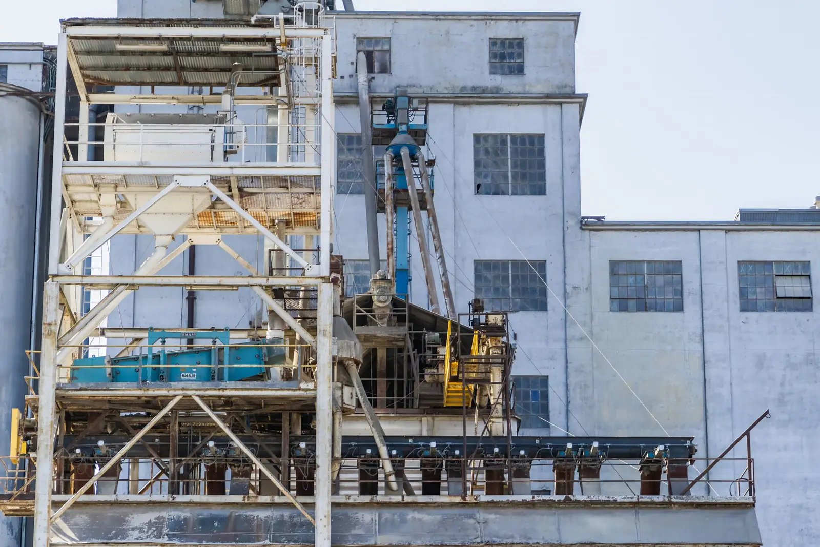 A processing plant’s conveyor gallery, screen deck, ductwork and silos against a plain white sky.